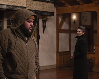 ASC_25_King Lear_007-Kent_Lear Kent in quilted, hooded jacket, zipped up to his beard stands left as Lear, turned in the opposite direction and wearing a black overcoat stands stiffly as he interrogates him.
